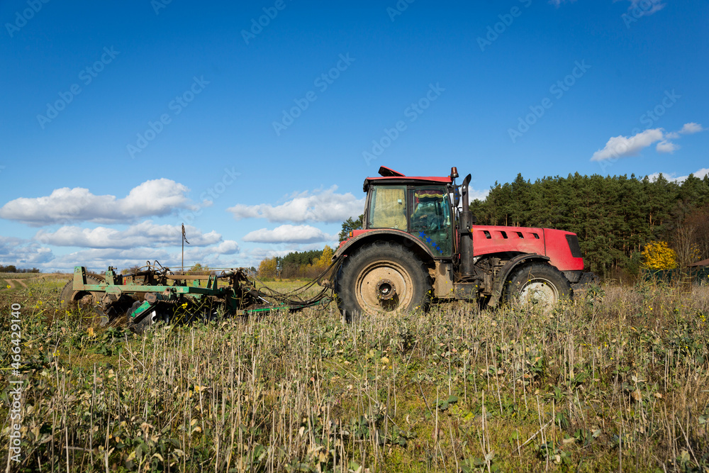 A farmer in a tractor, agricultural machinery, prepares the land with a cultivator. A modern red tractor in a field. Plowing a heavy tractor while cultivating agricultural work in a field with a plow. A farmer in a tractor, agricultural machinery, prepares the land with a cultivator. A modern red tractor in a field. Plowing a heavy tractor while cultivating agricultural work in a field with a plow.
