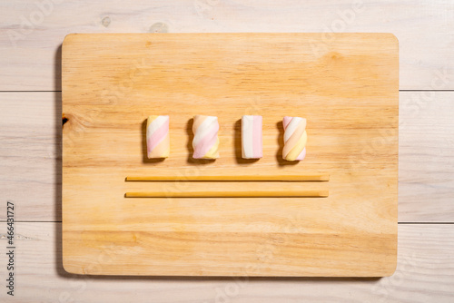 Marshmallows and chopsticks on wooden chopping board