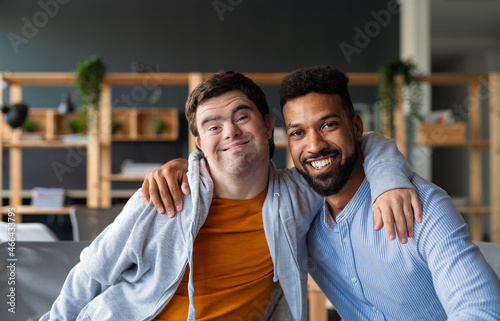 Young man with Down syndrome and his tutor with arms around looking at camera indoors at school photo