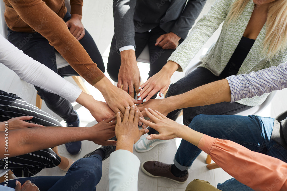 Stack of hands. Young motivated people fold their hands on each other symbolizing their unity and support. Close up of hands of multiracial people sitting in circle. Unity and teamwork concept.