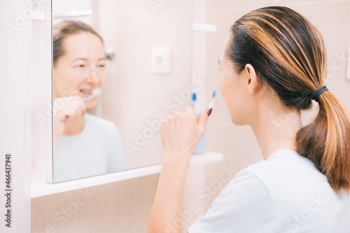 Woman with braces cleans her teeth with a toothbrush  before mirror. Dental and oral care. Selective focus on the person.