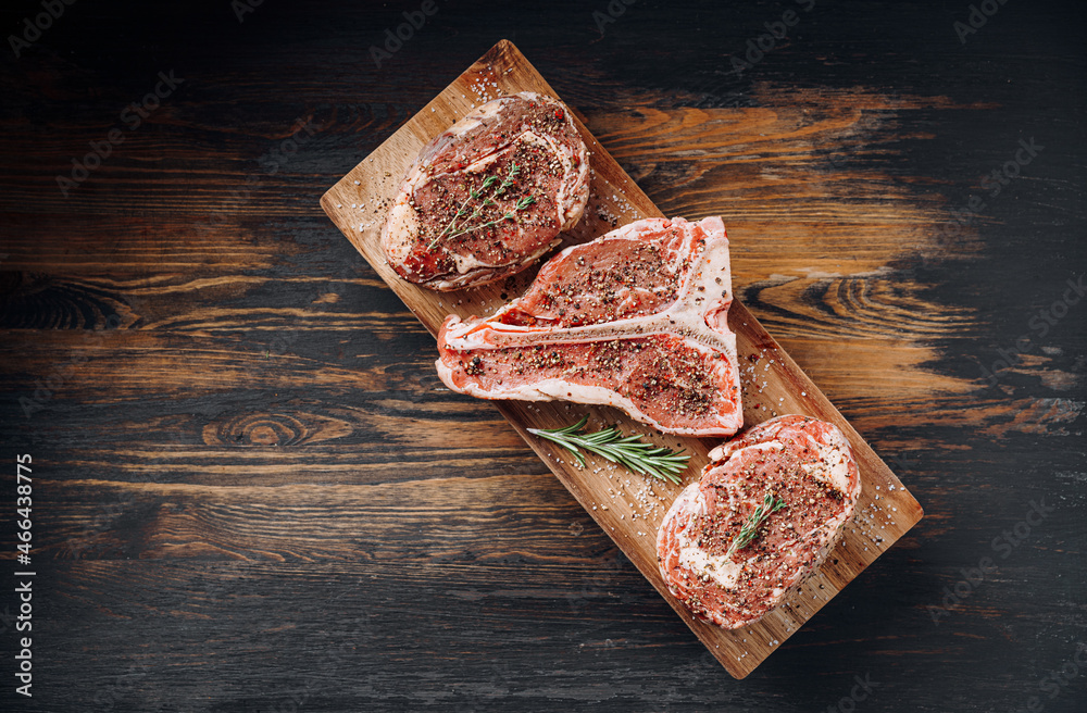three lovely raw marbled black Angus beef steaks flavored with a mixture of ground pepper and ready to cook and serve on a dark wooden background.