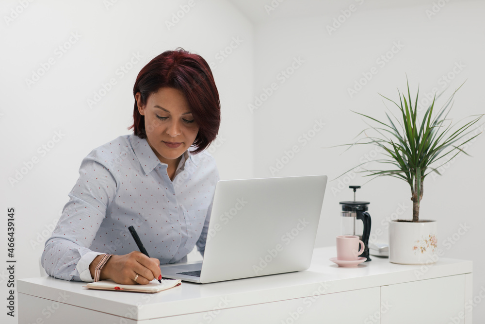 Businesswoman writing in note pad while working at home office