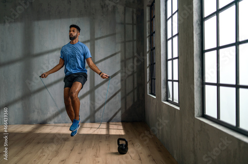 Young African American sportsman using jumping rope indoors, workout training concept.