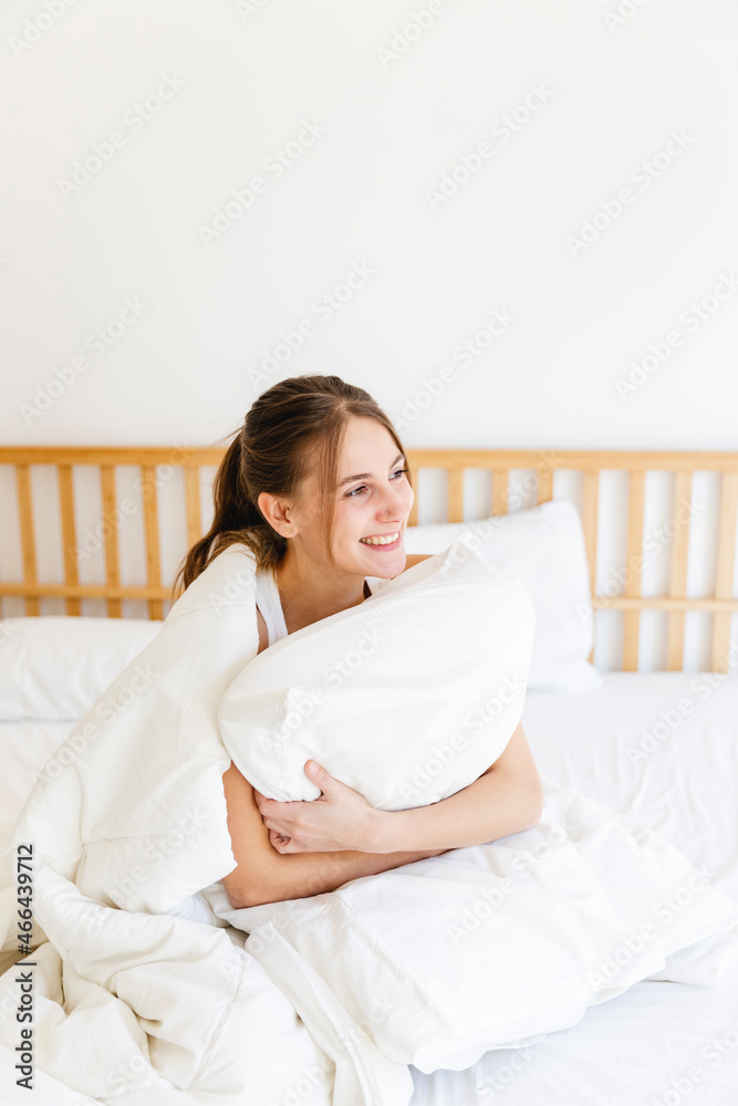 Smiling young woman embracing pillow while sitting on bed in bedroom Smiling young woman embracing pillow while sitting on bed in bedroom