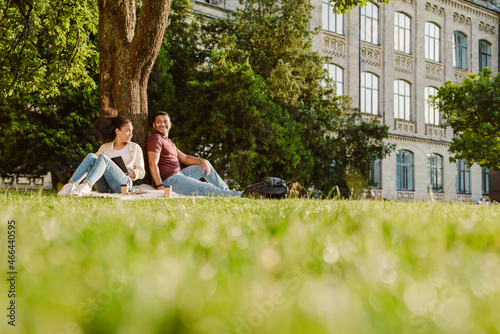 Multiracial students talking and laughing together while resting on grass