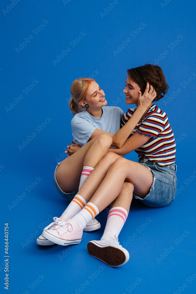 Lesbian couple smiling and hugging while sitting on floor together Lesbian couple smiling and hugging while sitting on floor together