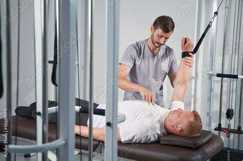 Man exercises on decompression trainer in with physiotherapist help