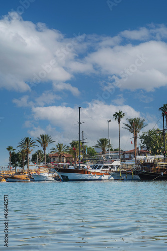 A small Mediterranean seaside town; Side. Boats, palm trees and sea under cloudy sky.