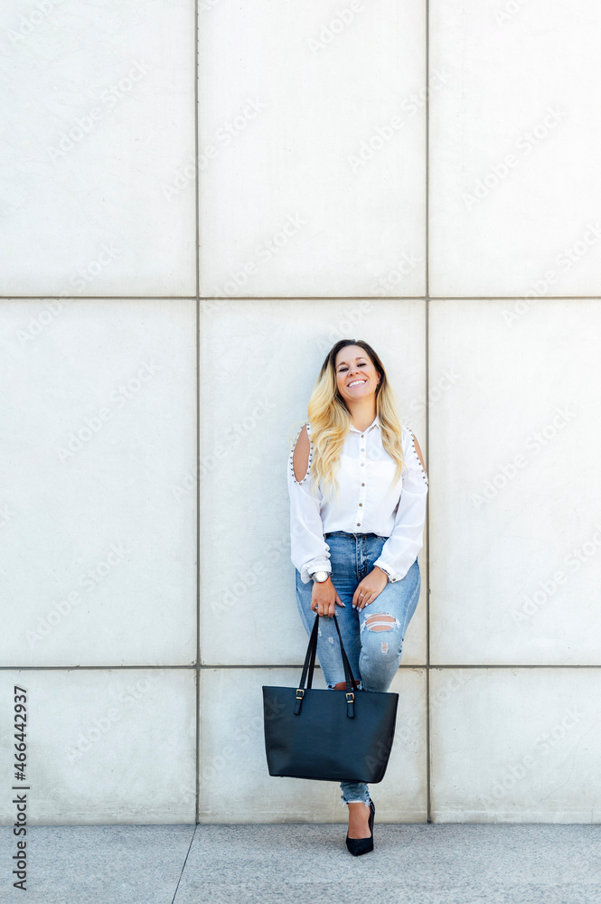 Smiling businesswoman with bag leaning on wall