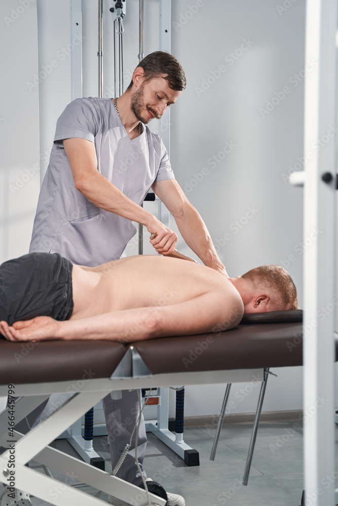 Fototapeta premium Man doctor back massages with steel scraper for patient with back pain