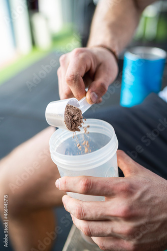 Sportsman putting protein powder in shaker after working out photo