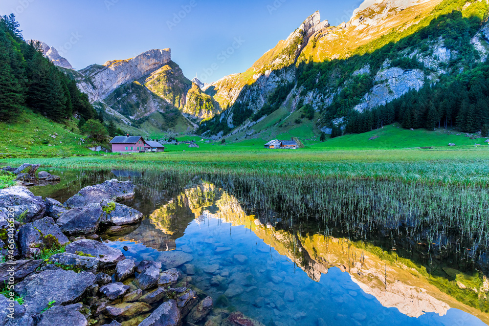 Mountains reflecting in clear water of Seealpsee lake at dawn with secluded huts in background Mountains reflecting in clear water of Seealpsee lake at dawn with secluded huts in background