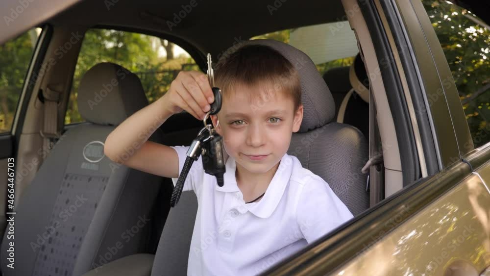 Portrait of a little boy in a white T-shirt sitting behind the wheel in a car with keys in his hands.