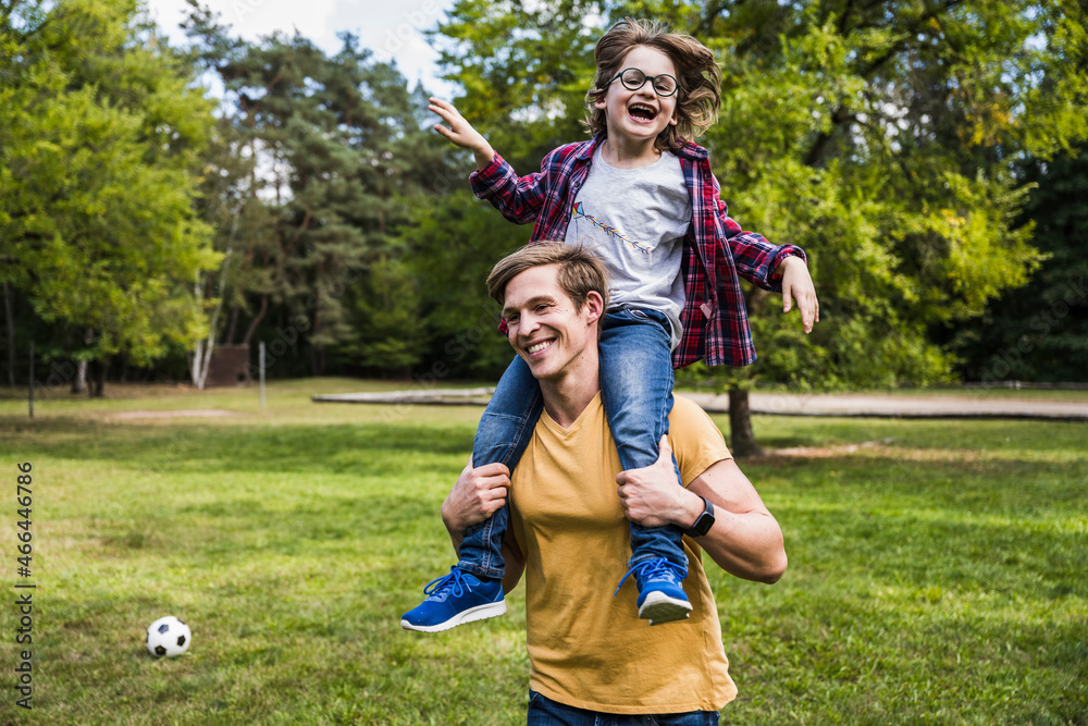 Happy man carrying playful boy on shoulders at park Happy man carrying playful boy on shoulders at park