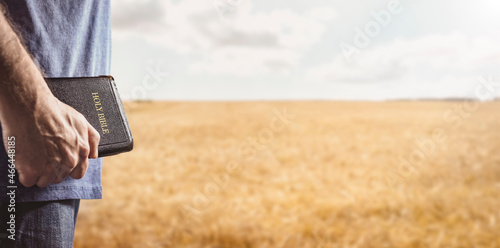 Tableau sur toile Christian man holding the Holy Bible in a field background