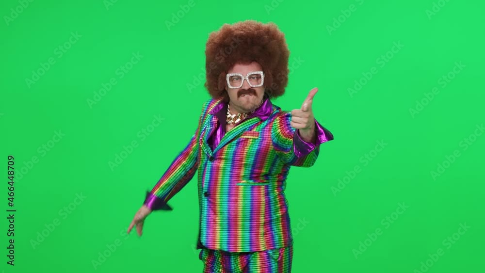 Retro dude in a funny wig and multicolored suit is dancing a funny spinning dance on a green background, a festive mood, a retro disco man is having fun at a new year's party.