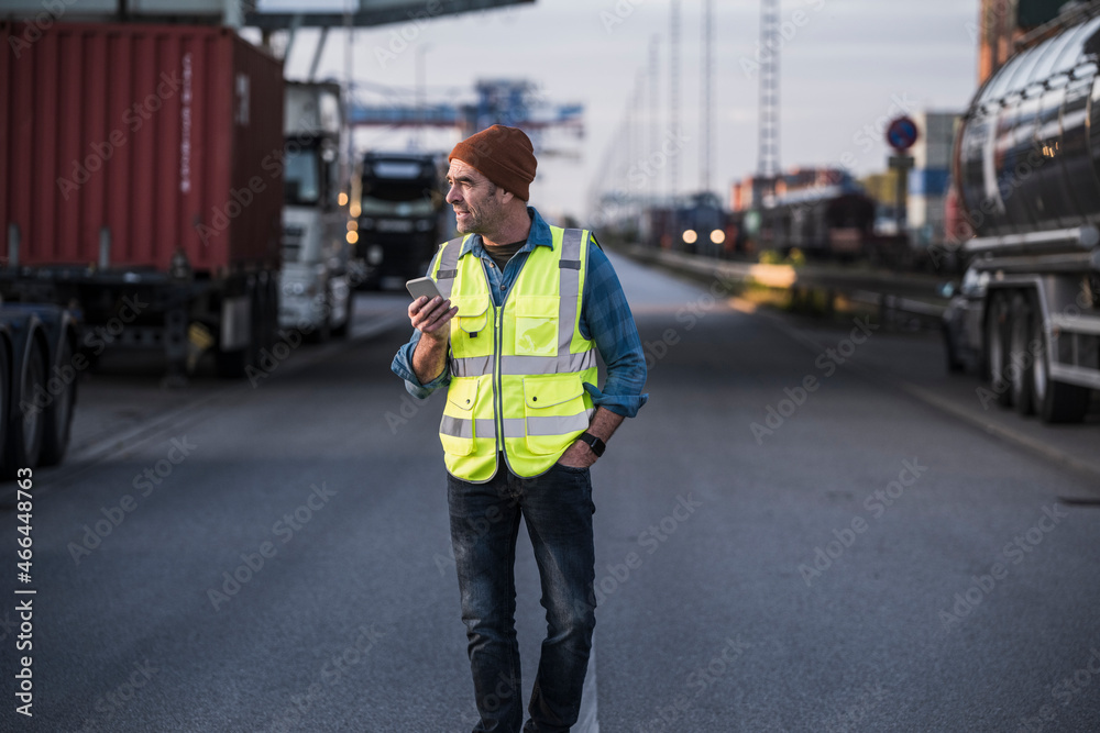 Male truck driver with smart phone walking on street at industry Male truck driver with smart phone walking on street at industry