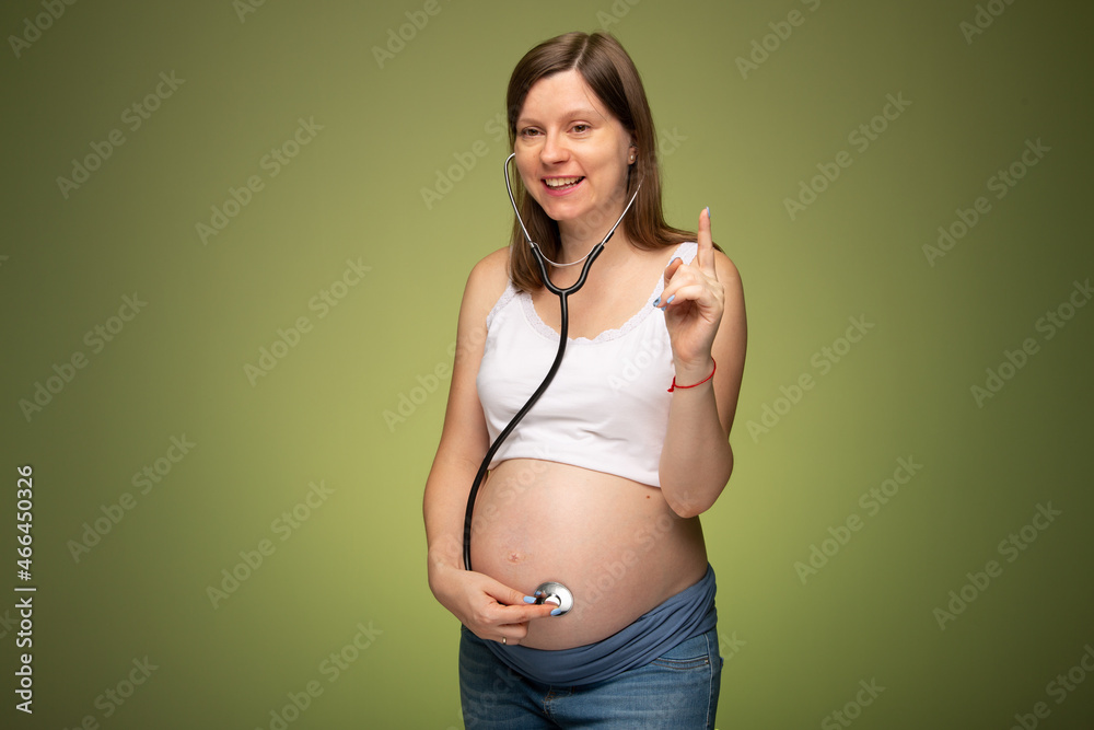 Pregnant woman with stethoscope trying to hear her baby heartbeat by herself. Worrying in pregnancy. Woman with tammy preparing for the birth of the baby. Pregnant woman with stethoscope trying to hear her baby heartbeat by herself. Worrying in pregnancy. Woman with tammy preparing for the birth of the baby.