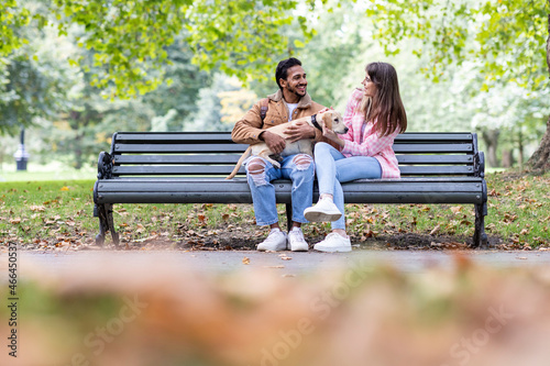 Happy young couple with dog sitting on bench in public park