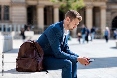 Male professional using mobile phone while sitting by backpack photo