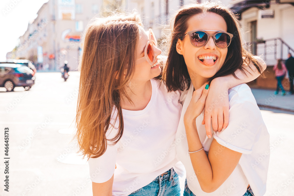 Two young beautiful smiling hipster female in trendy summer white t-shirt clothes and jeans.Sexy carefree women posing on the street background. Positive models having fun, hugging and going crazy Two young beautiful smiling hipster female in trendy summer white t-shirt clothes and jeans.Sexy carefree women posing on the street background. Positive models having fun, hugging and going crazy