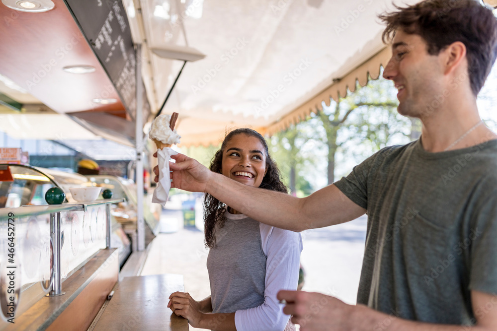 Smiling woman looking at friend buying ice cream at park Smiling woman looking at friend buying ice cream at park