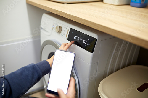 Woman operating washing machine through smart phone in utility room at home photo