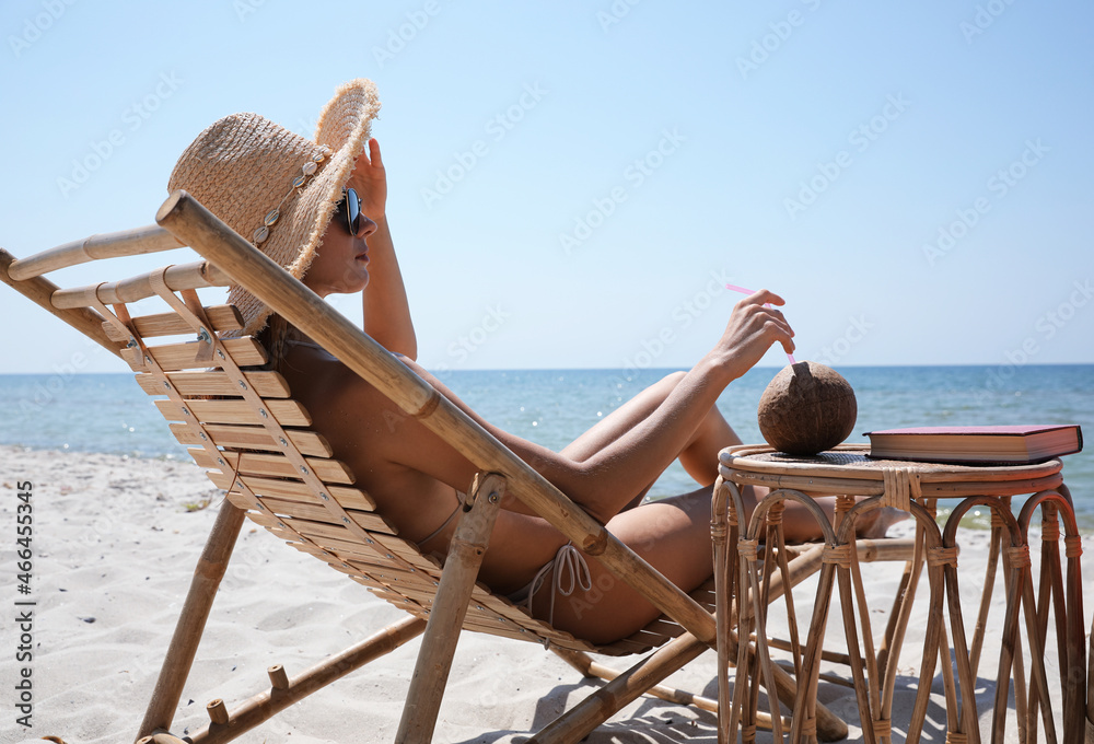 Woman with cocktail resting in wooden sunbed on tropical beach
