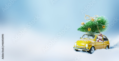 Retro toy car driven by a snowman carrying christmas tree on a roof .