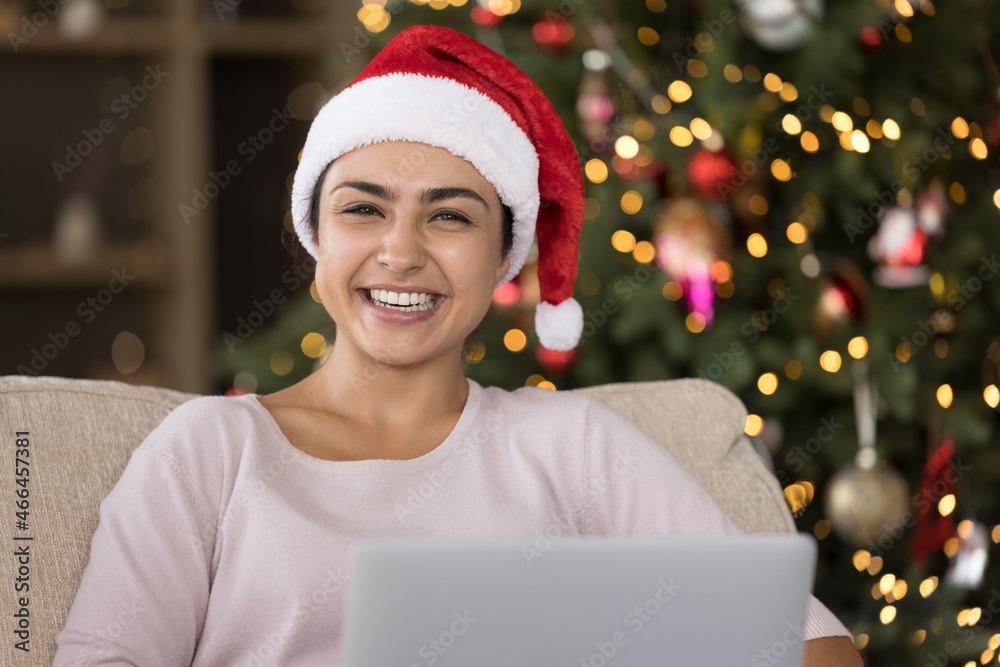 Portrait of joyful laughing young Indian woman in festive red hat using computer, feeling excited reading New year congratulations or watching funny Christmas movies online, resting on cozy sofa. Portrait of joyful laughing young Indian woman in festive red hat using computer, feeling excited reading New year congratulations or watching funny Christmas movies online, resting on cozy sofa.