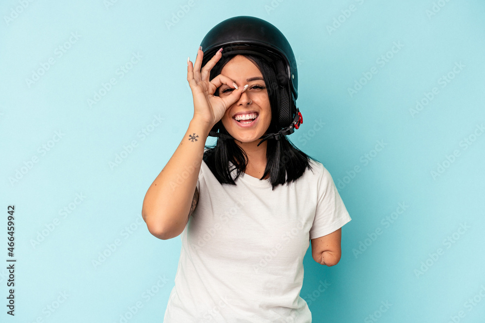 Young caucasian woman with one arm wearing a motorcycle helmet isolated o blue background excited keeping ok gesture on eye.