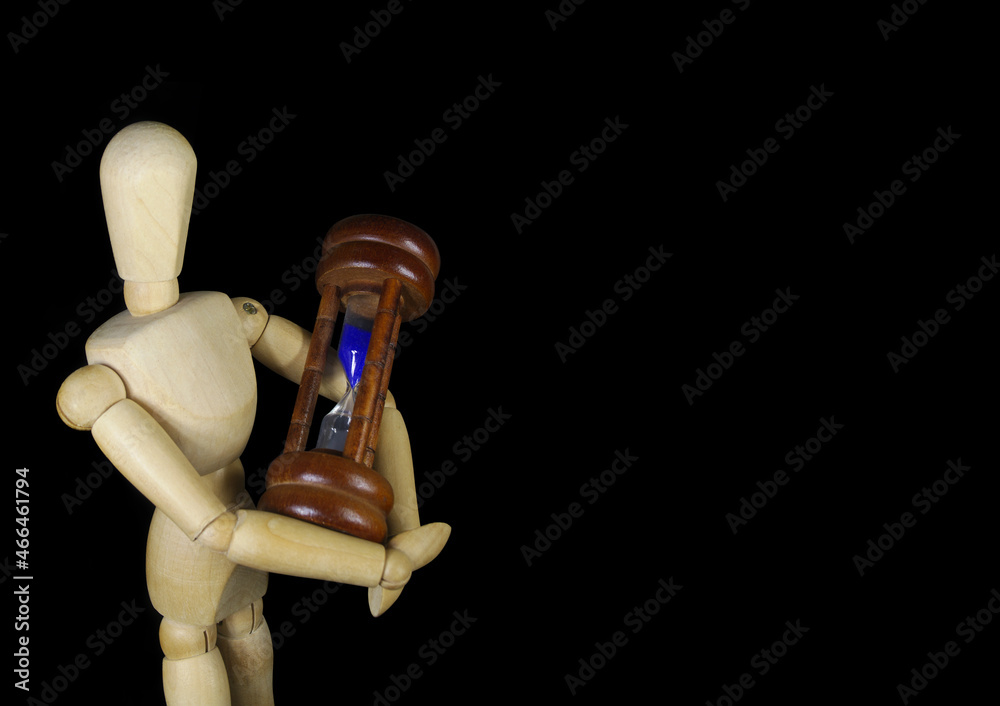 Wooden mannequin holds hourglass isolated on black with copy space for text, lifetime and deadline concept. Wooden mannequin holds hourglass isolated on black with copy space for text, lifetime and deadline concept.