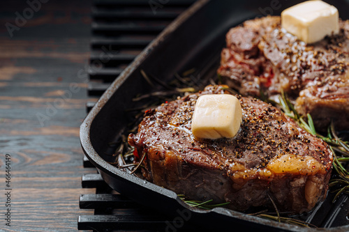 cooking sumptuous steaks in a grill pan with butter spreading over the steak seasoned with ground pepper and salt with rosemary sprigs