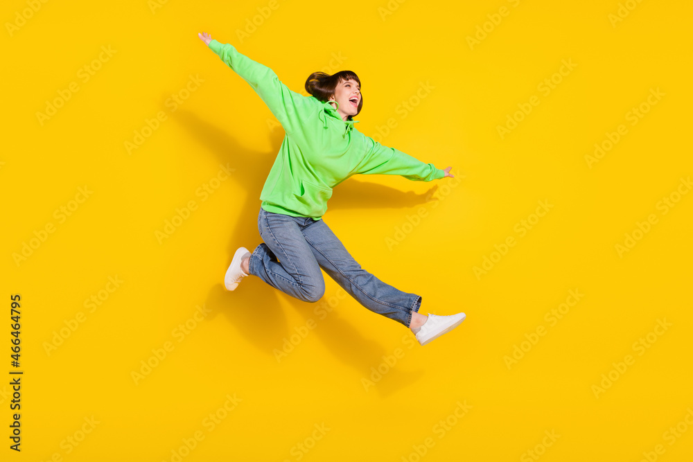 Full length photo of cheerful happy young woman jump up hands wings isolated on shine yellow color background