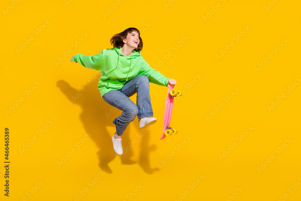 Full length body size view of pretty cheery girl jumping riding skate having fun spare time isolated over bright yellow color background