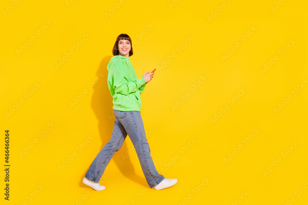 Full length body size profile side view of attractive cheerful girl using device going isolated over bright yellow color background Full length body size profile side view of attractive cheerful girl using device going isolated over bright yellow color background