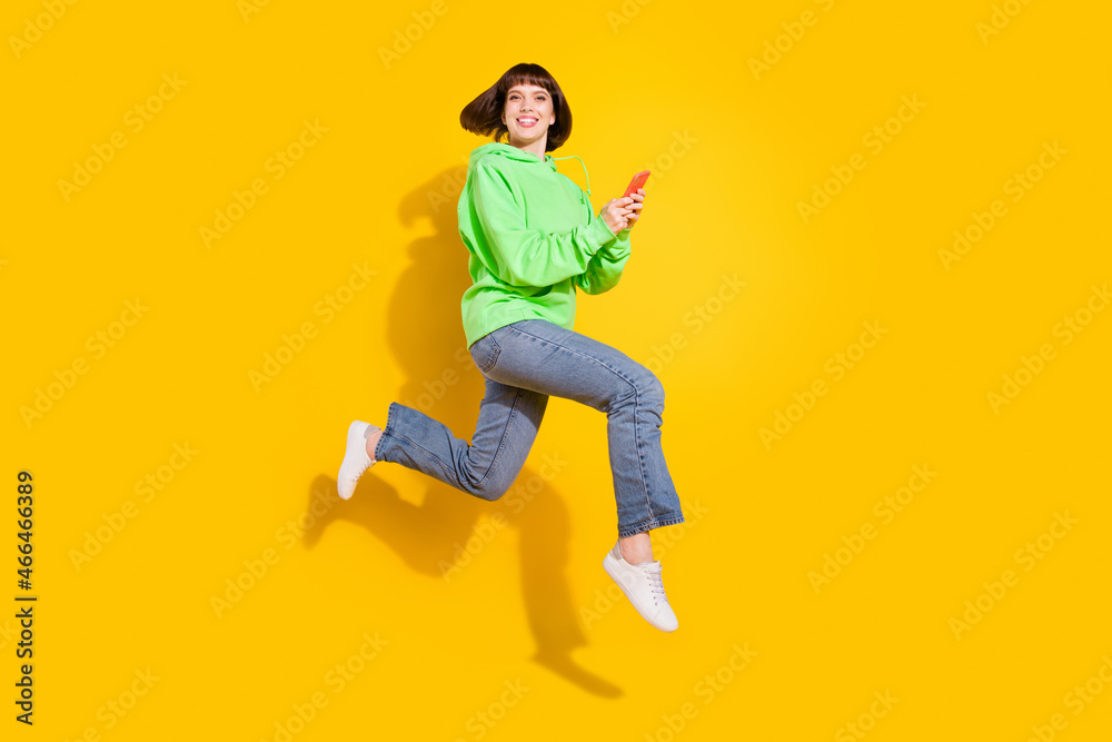 Full length body size view of attractive cheery girl jumping using gadget 5g isolated over bright yellow color background