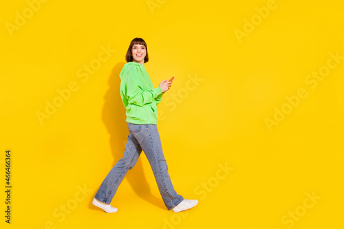 Full length body size profile side view of attractive cheerful girl using device going isolated over bright yellow color background
