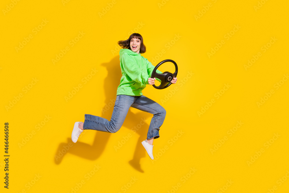 Fototapeta premium Full length body size view of nice cheery girl jumping holding steering wheel ride isolated over bright yellow color background