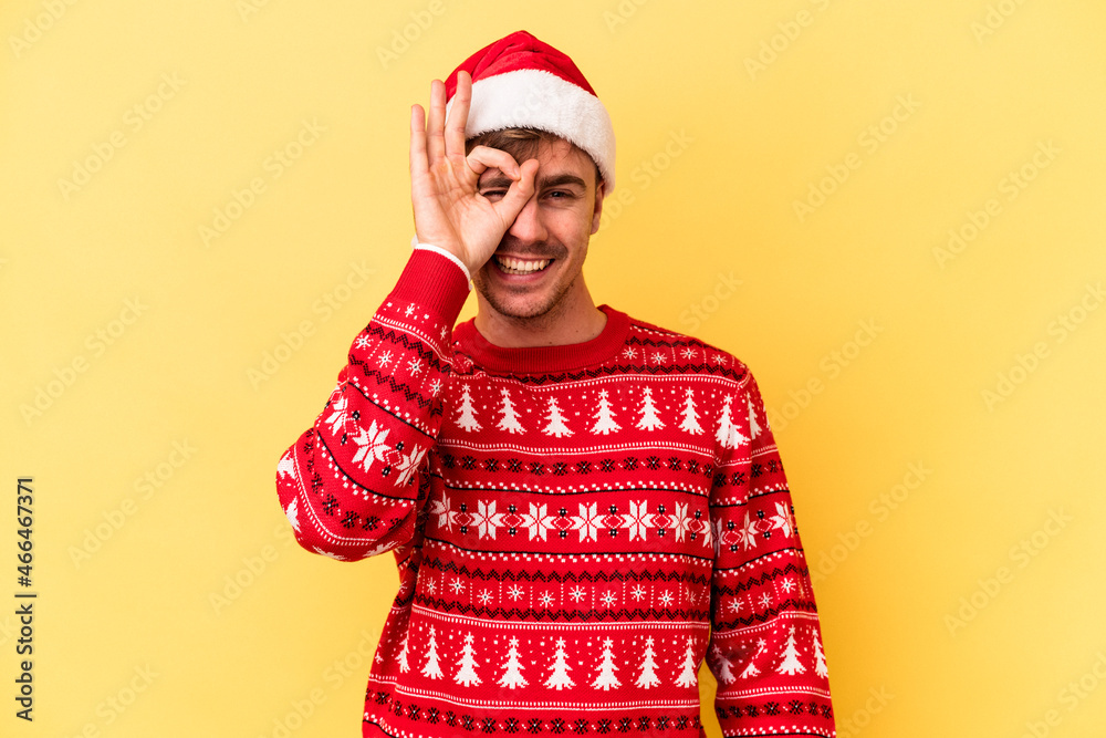 Young caucasian man celebrating Christmas isolated on yellow background excited keeping ok gesture on eye. Young caucasian man celebrating Christmas isolated on yellow background excited keeping ok gesture on eye.