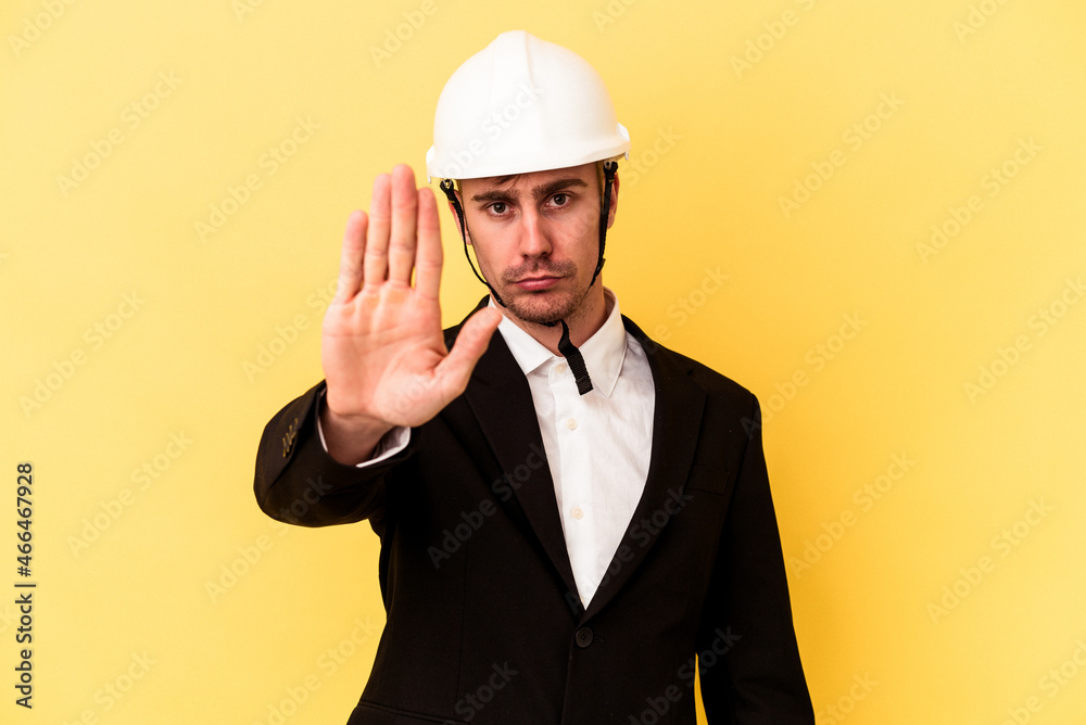 Young architect caucasian man isolated on yellow background standing with outstretched hand showing stop sign, preventing you.
