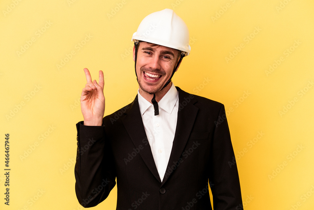Young architect caucasian man isolated on yellow background joyful and carefree showing a peace symbol with fingers. Young architect caucasian man isolated on yellow background joyful and carefree showing a peace symbol with fingers.