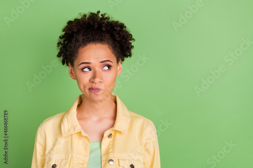 Photo of unsure millennial brunette lady look empty space wear yellow shirt isolated on green color background