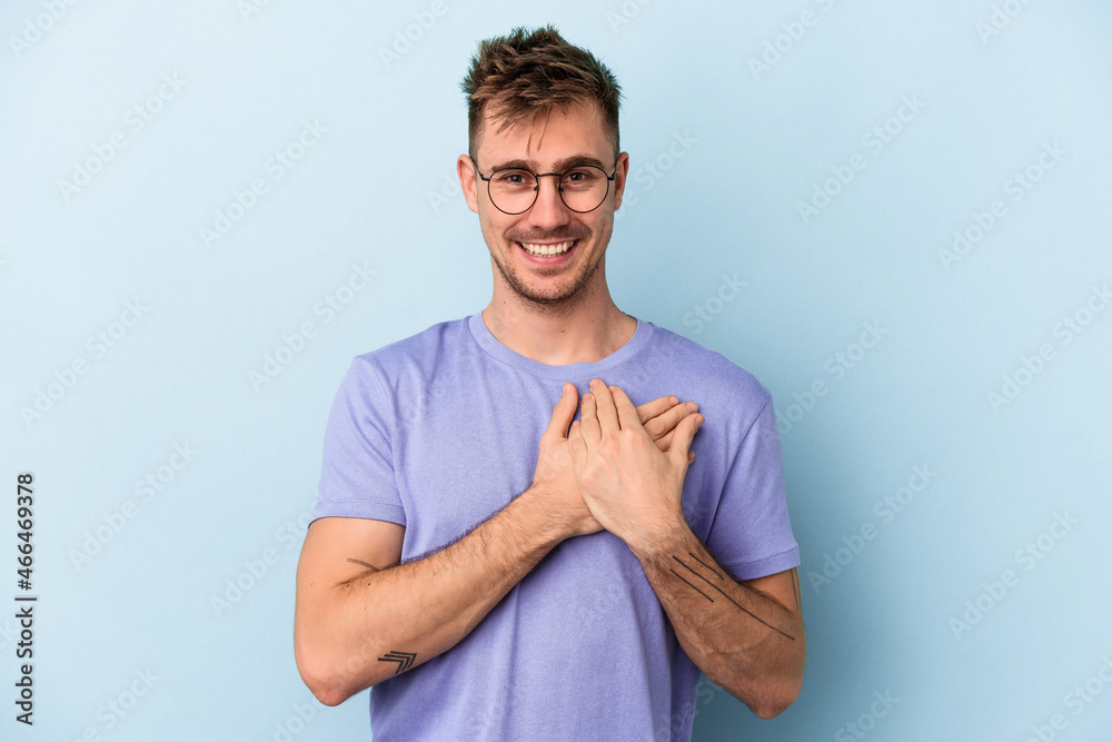 Young caucasian man isolated on blue background laughing keeping hands on heart, concept of happiness.