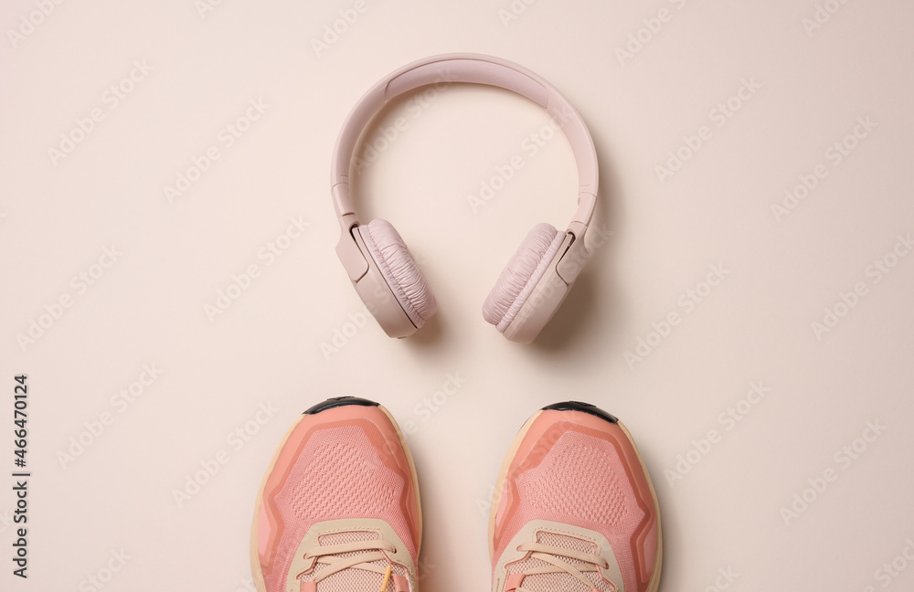 pair of pink textile sneakers, wireless headphones on a beige background. Set for sports pair of pink textile sneakers, wireless headphones on a beige background. Set for sports