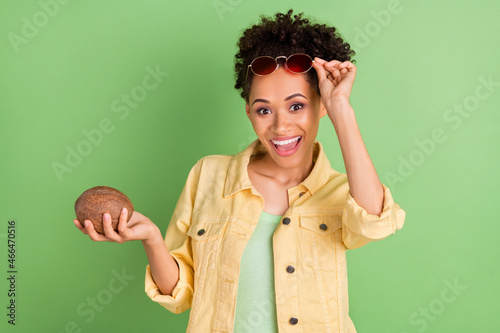 Photo of impressed young brunette lady hold coconut wear eyewear yellow shirt isolated on green color background