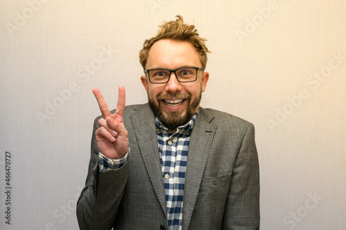 Funny nerdy weirdo caucasian bearded man with eyeglasses in a suit posing with peace sign for a photo  photo