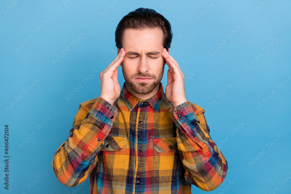 Photo of charming tired young guy dressed checkered shirt arms temples having pain isolated blue color background Photo of charming tired young guy dressed checkered shirt arms temples having pain isolated blue color background