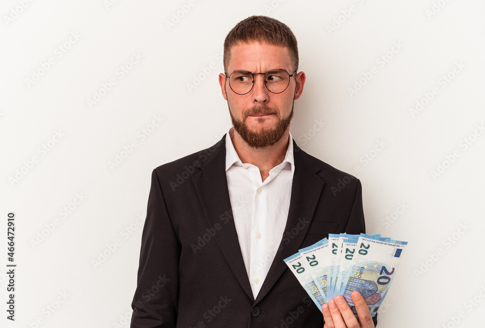 Young business caucasian man holding banknotes isolated on white background confused, feels doubtful and unsure. Young business caucasian man holding banknotes isolated on white background confused, feels doubtful and unsure.